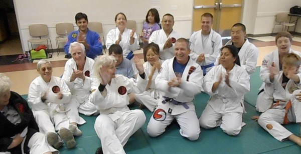 Group of martial artists in white uniforms clapping and smiling.