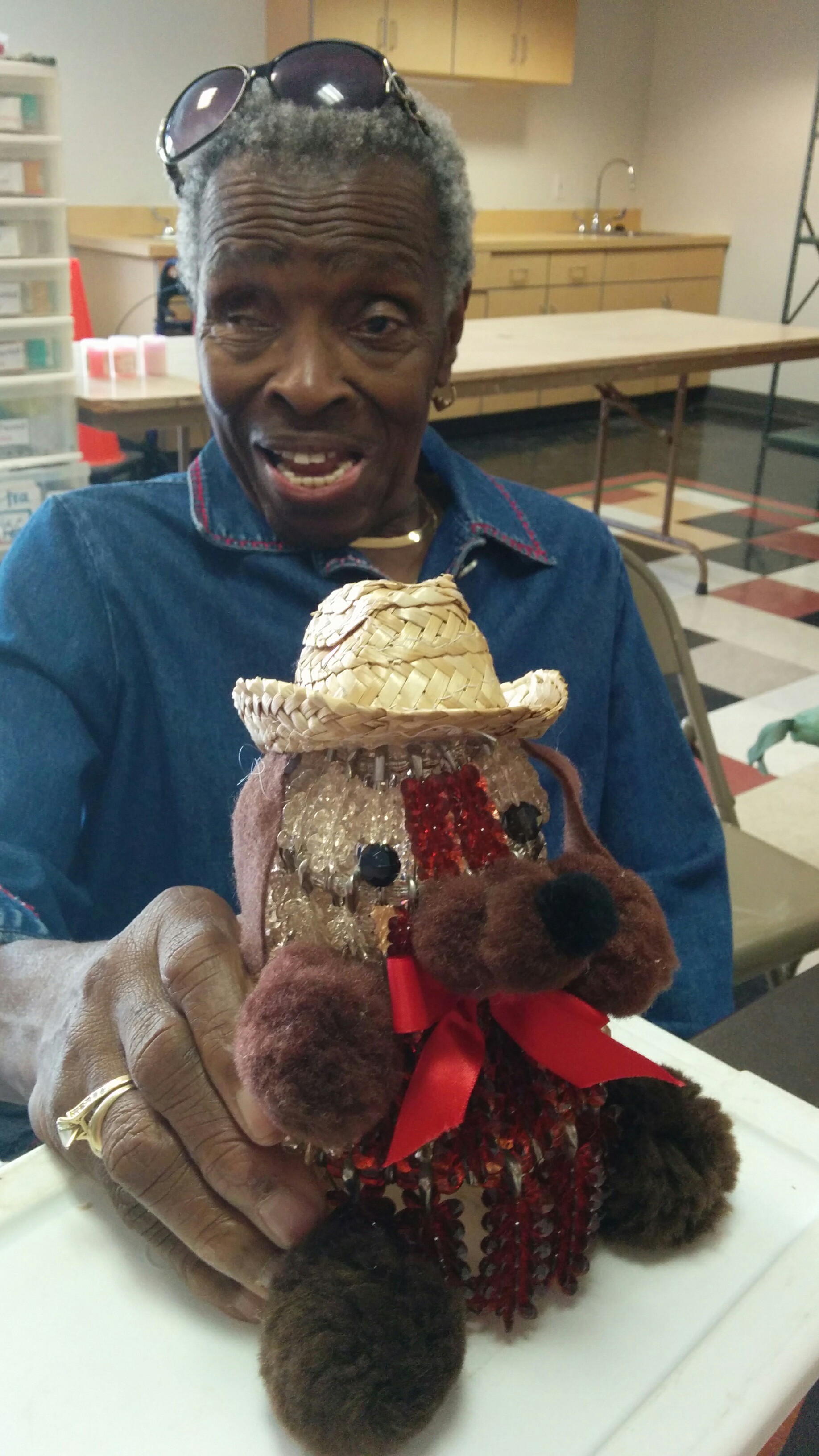 Man smiling behind a plush moose wearing a cowboy hat and red scarf.