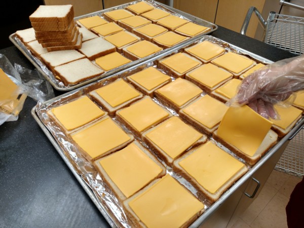 Multiple trays of sliced bread topped with cheese slices.