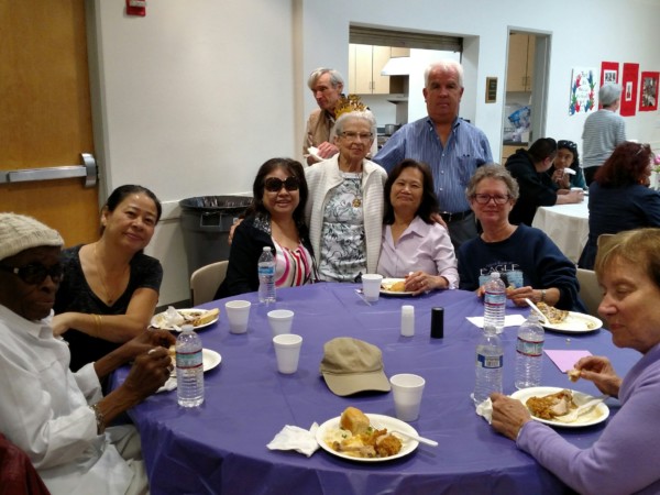 A group of people smiling around a table with food and drinks.