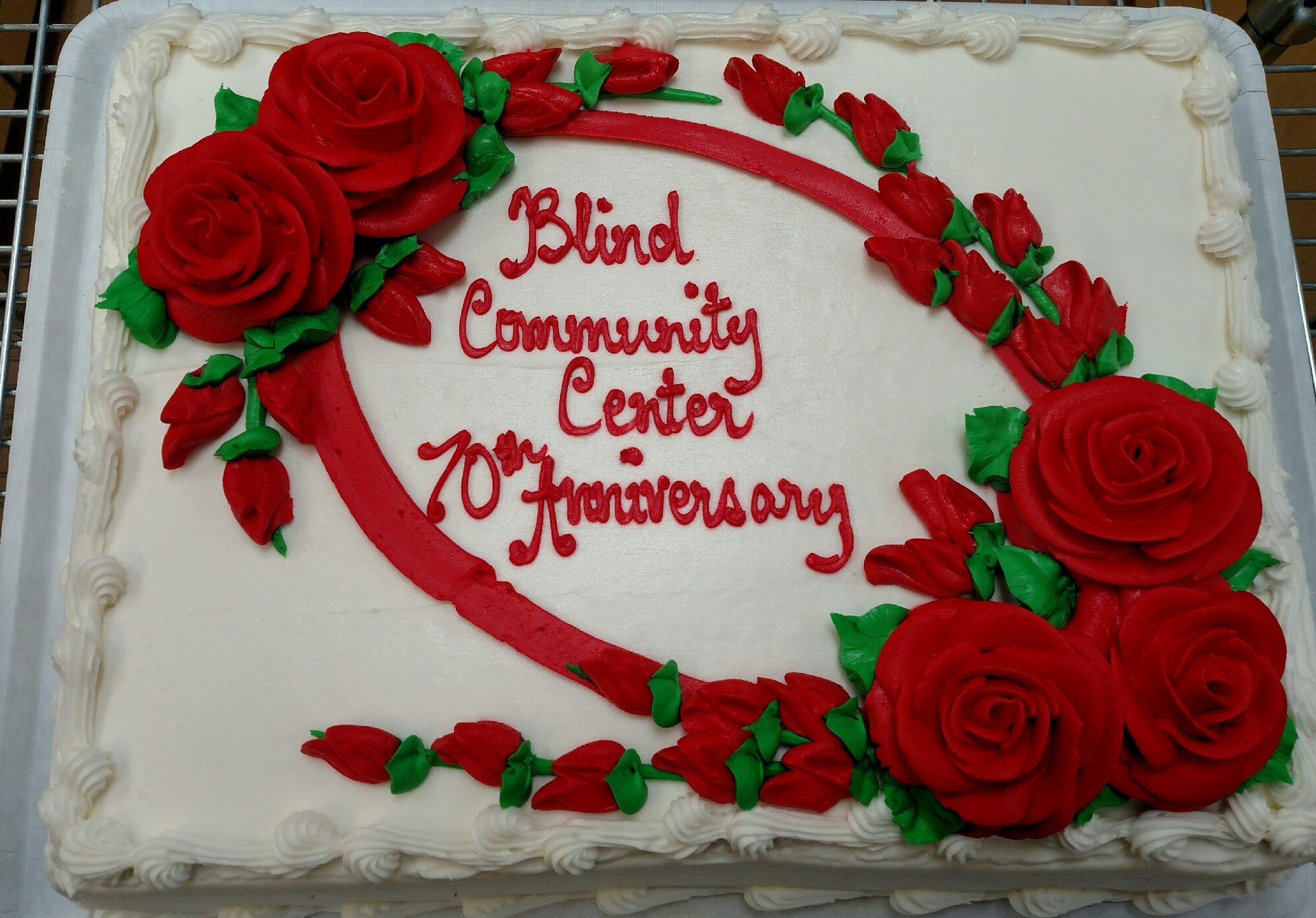 A cake celebrating the Blind Community Center's 70th anniversary with red roses.