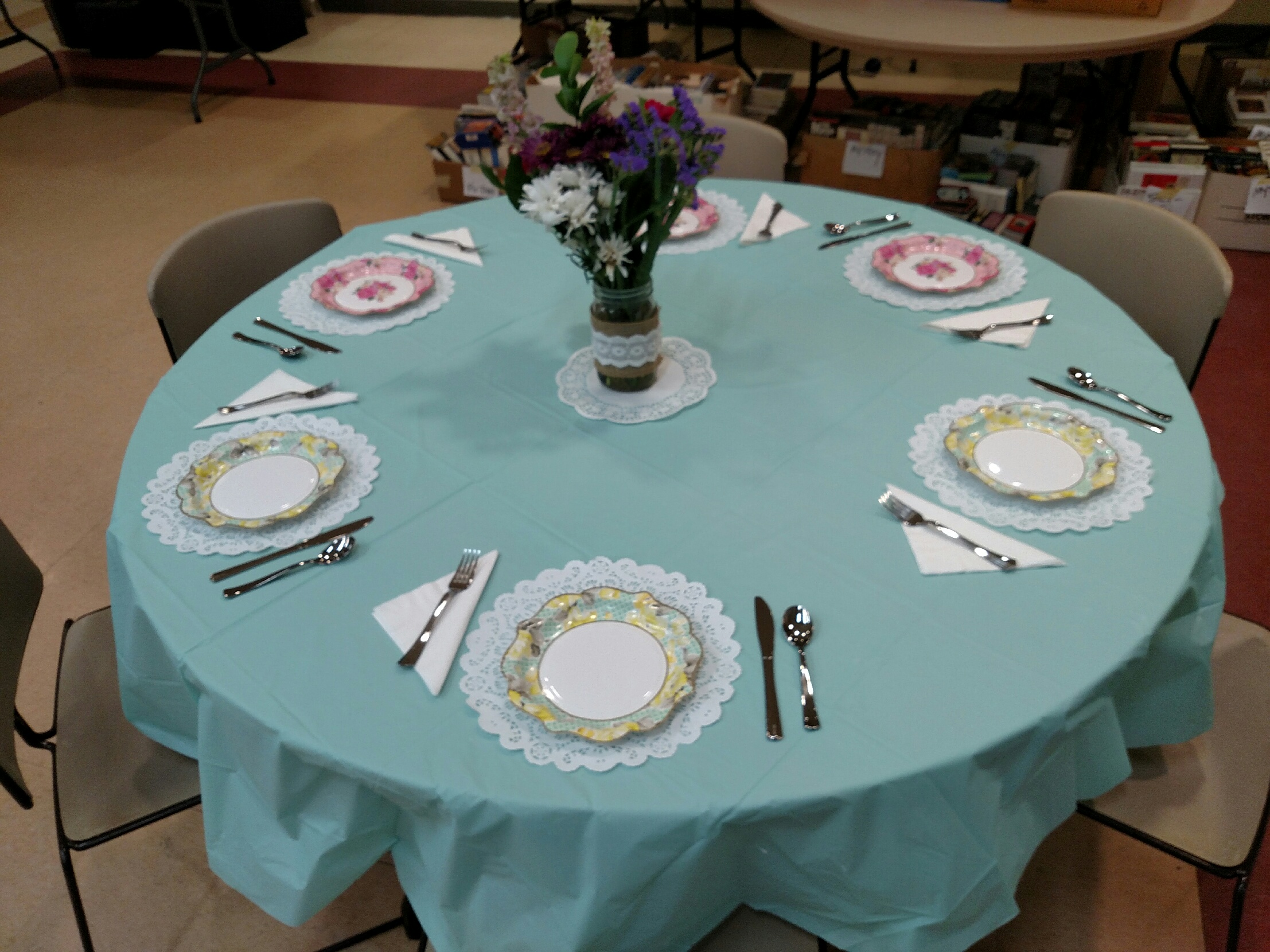 Elegant round table set for six with floral centerpiece and teal tablecloth.