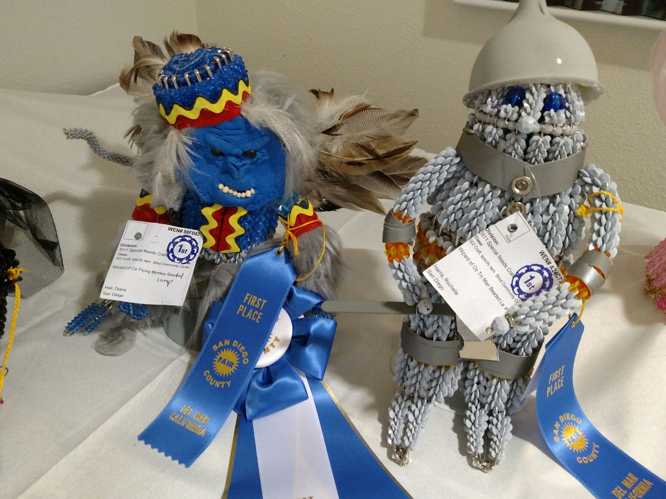 Two handcrafted dolls, a colorful blue one and a silver beaded one, each with award ribbons.