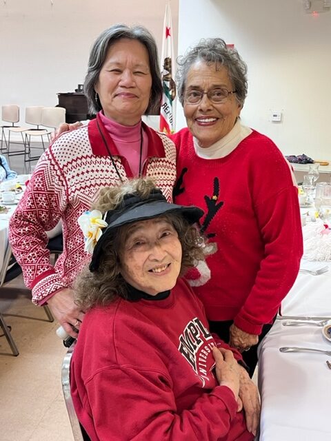 Three joyful women in festive red sweaters posing indoors.